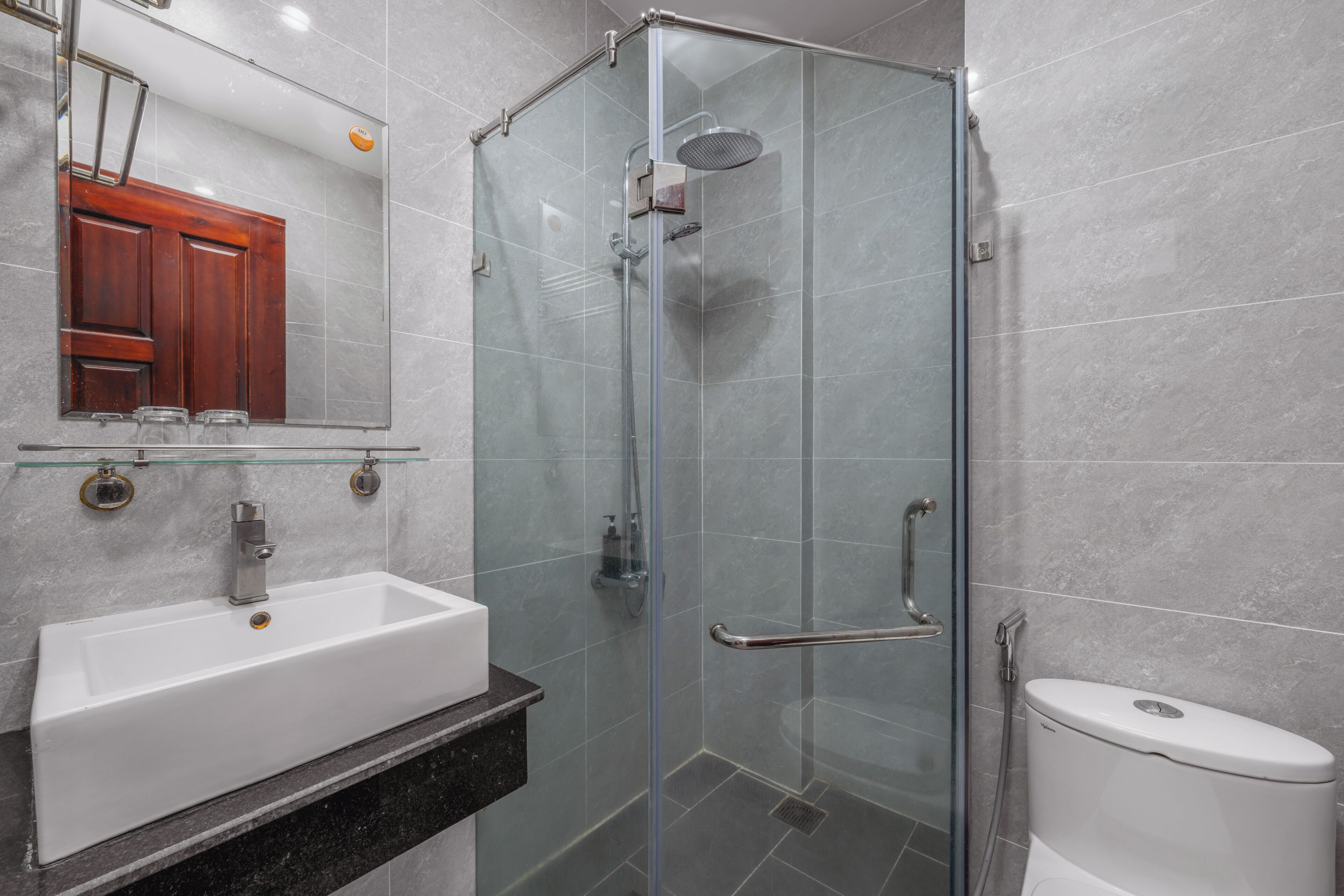 Un baño moderno con ducha de vidrio, un lavamanos blanco y un inodoro.
