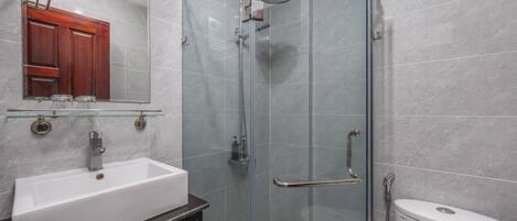 Un baño moderno con ducha de vidrio, un lavamanos blanco y un inodoro.