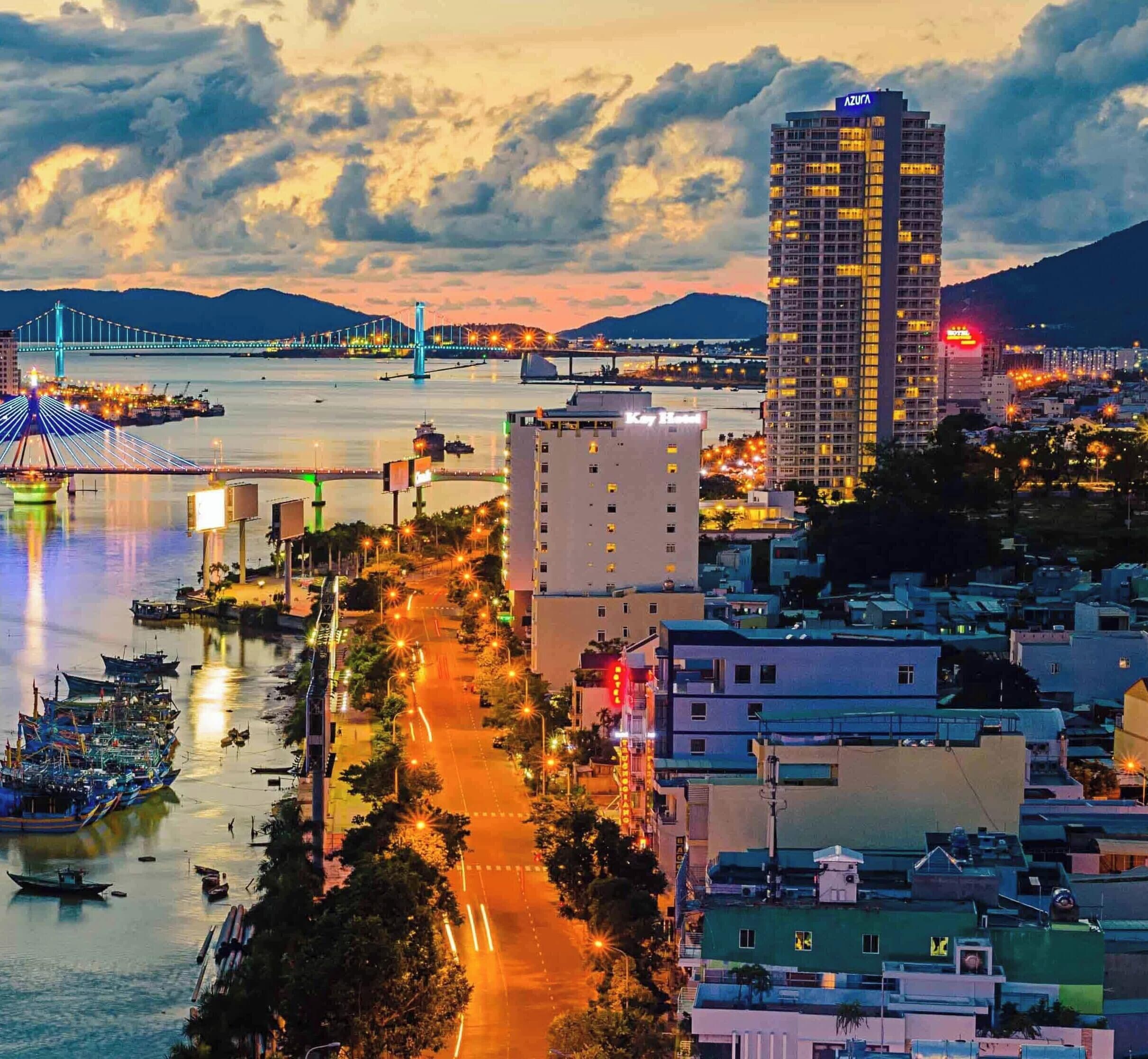 A coastal cityscape with a prominent bridge, a high-rise hotel, and a waterfront promenade.