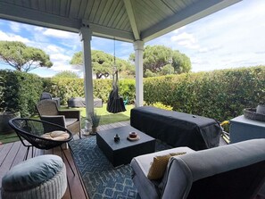 Eine Außenpatio mit überdachter Sitzgelegenheit, darunter eine Couch, Stühle und ein kleiner Tisch.