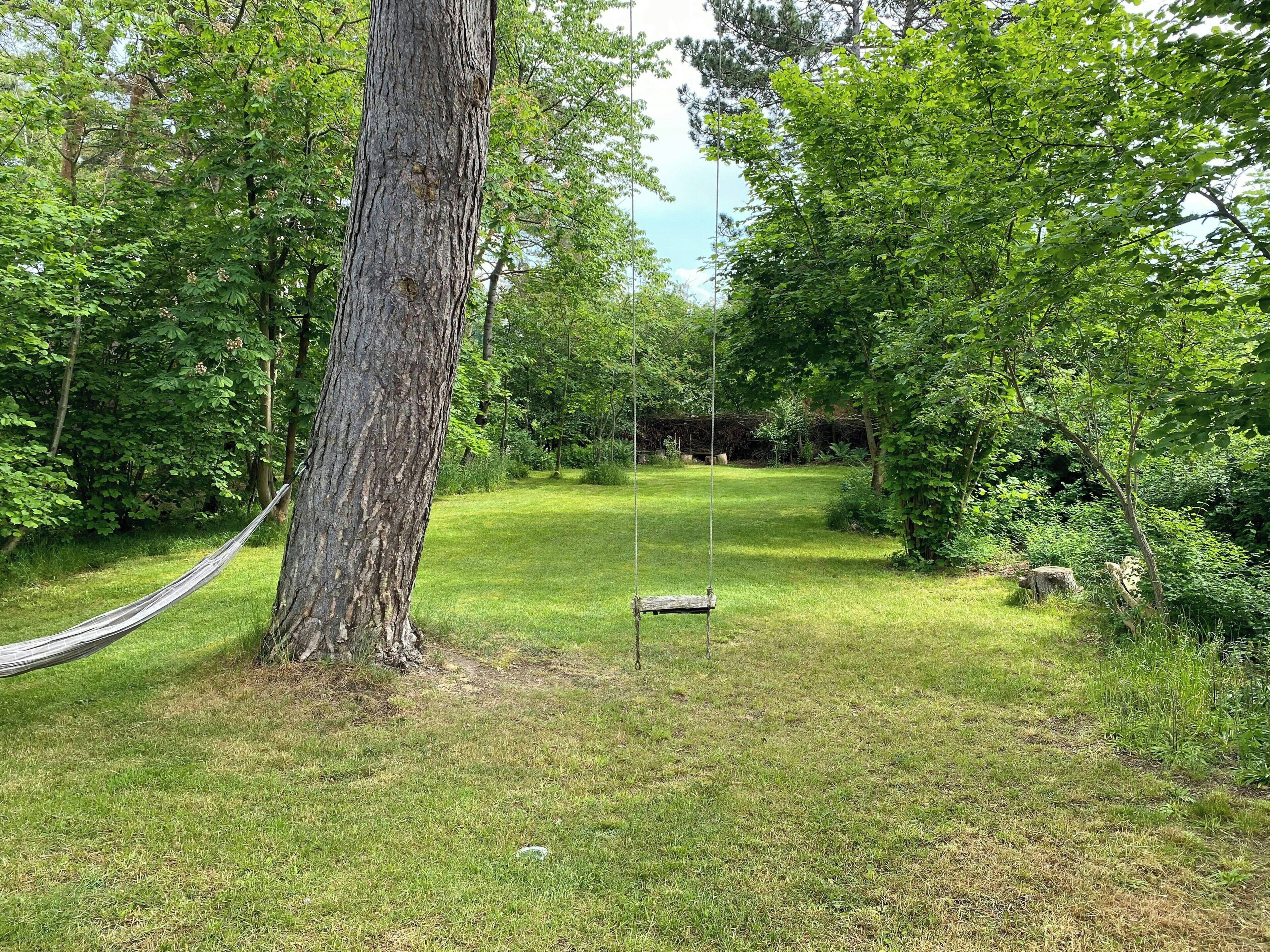 En hängmatta som är fastknuten i ett träd på en gräsyta, med en gunga i bakgrunden.