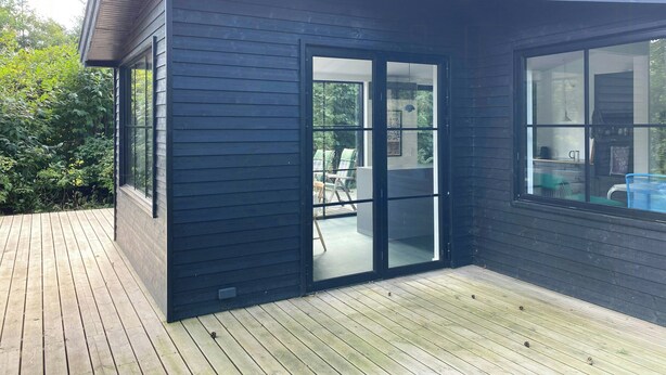 Ein modernes Haus mit dunkler Fassade, großen Glasüren und einer Holzterrasse.