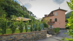 Ein zweigeschossiges Haus mit einer Steinmauer, einem gepflasterten Zugangsweg und einem grünen Rasen.
