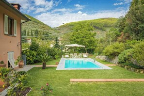 Ein Swimmingpool mit Sonnenschirm, umgeben von einer gepflegten Rasenfläche und einem Hügel im Hintergrund.