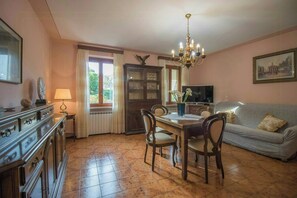 Ein Essbereich mit Holztisch, Stühlen, einer Deckenleuchte, einem Fernseher und einer Couch.