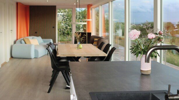 Un comedor moderno con una mesa de madera, sillas negras y un florero con flores.