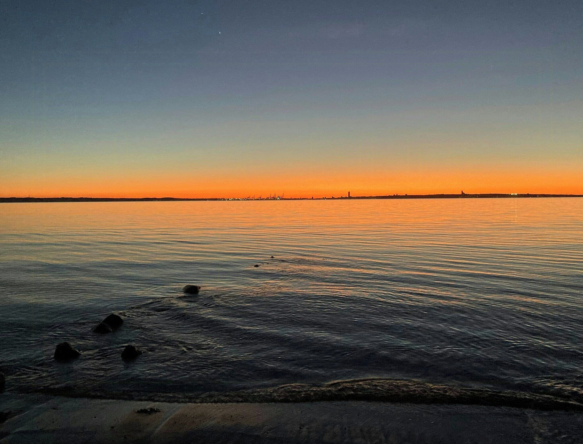 A calm body of water with a distant shoreline silhouette.