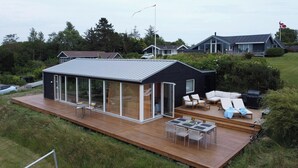 Una casa moderna con un amplio patio cubierto de vidrio, mobiliario exterior y una terraza.