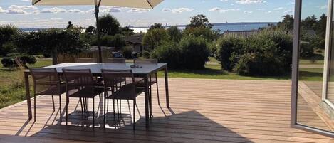 A wooden deck with a table and chairs, an umbrella, and a view of the sea.