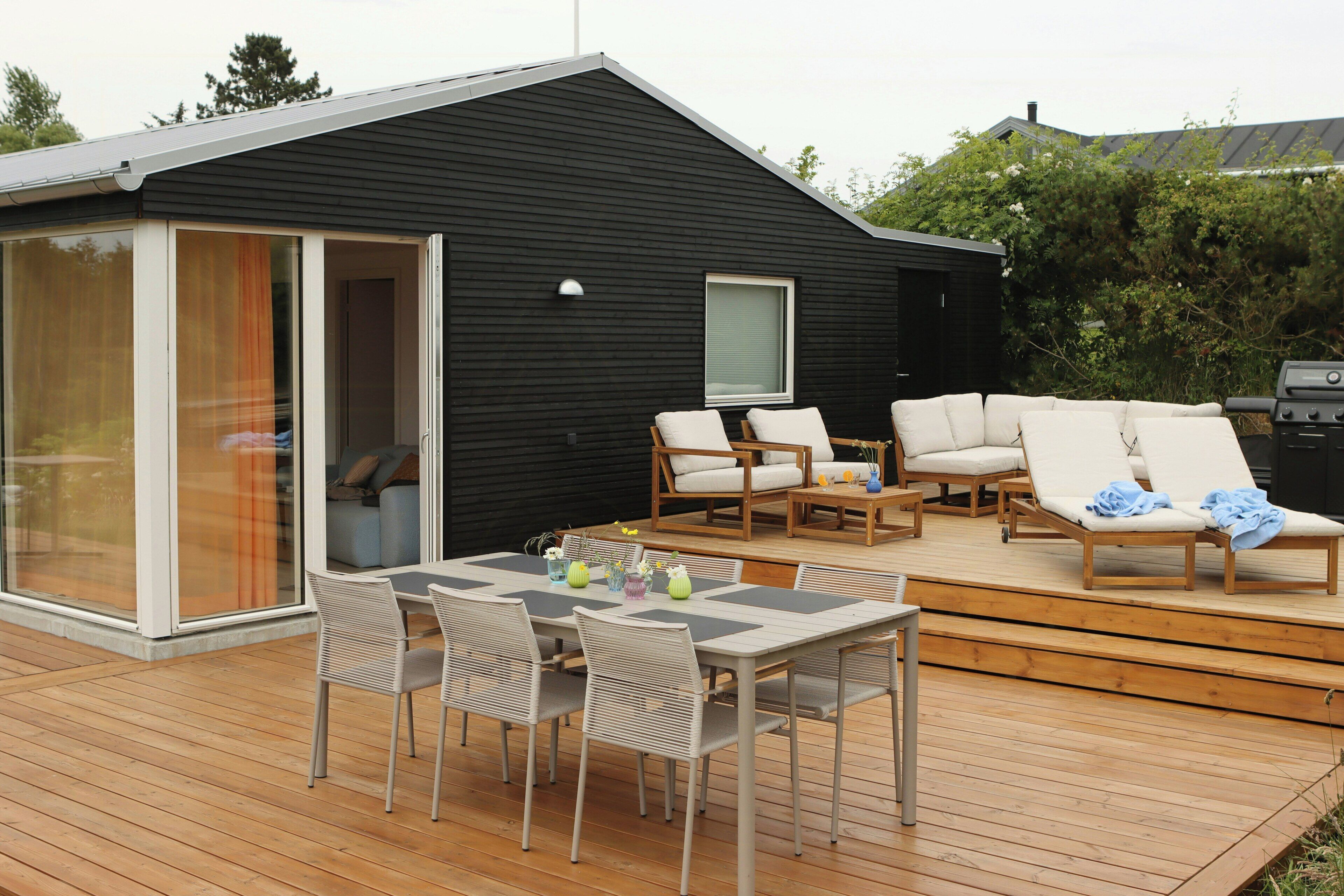 A modern outdoor deck with a dining table, chairs, lounge chairs, and a grill.