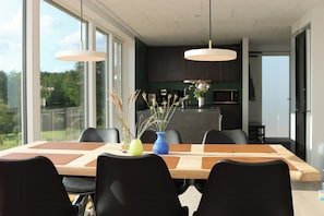 Een moderne keuken met donkere kastjes, een roestvrijstalen koelkast en een eethoek met een houten tafel en zwarte stoelen.