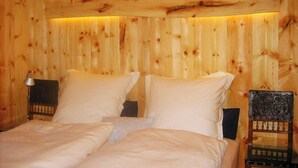 Una habitació de fusta amb un llit, dues taules de nit i una cadira decorativa.