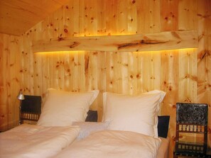 Ein Zimmer mit Holzboden, einem Bett, zwei Nachttischen und einem dekorativen Sessel.