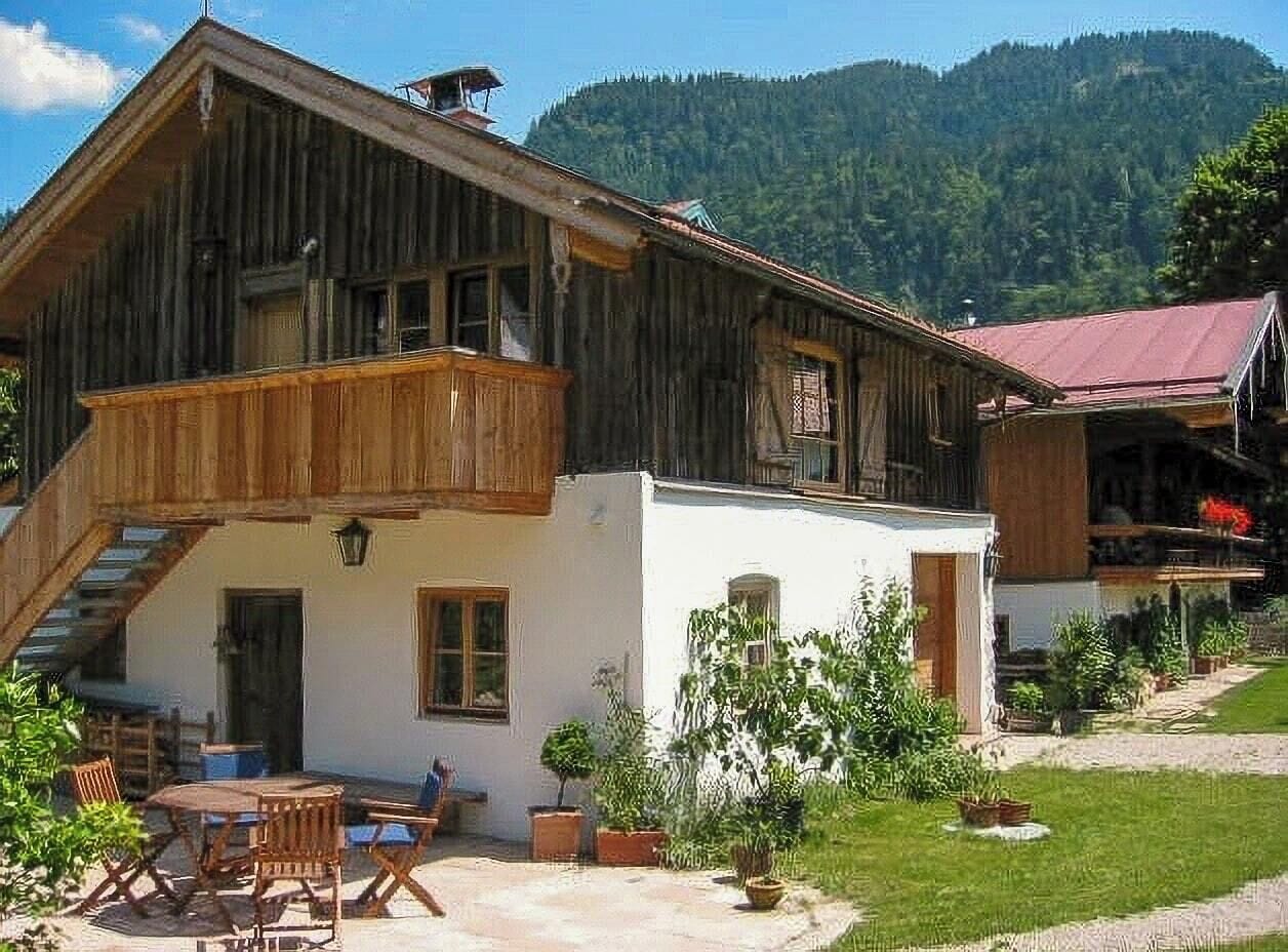 Ein Holzgebäude mit einem Balkon, einem weißen Anbau und einer Treppe, die zu der oberen Etage führt.