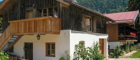 Ein Holzgebäude mit einem Balkon, einem weißen Anbau und einer Treppe, die zu der oberen Etage führt.