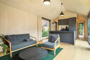 Ein modernes Interieur mit einer Couch, einem Sessel und einem runden Couchtisch in einem hellen Raum mit Holzwänden und einer Küchenzeile.