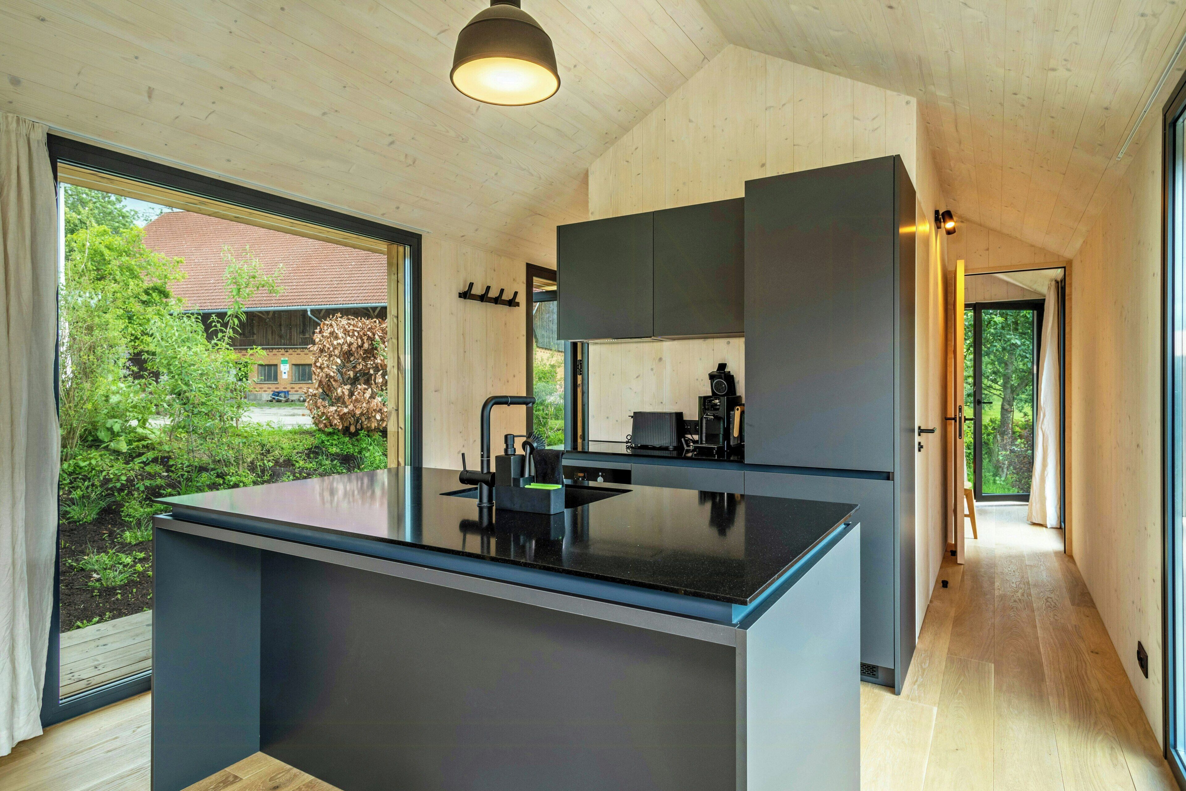 A modern kitchen with a central island, wooden ceiling, and large windows.