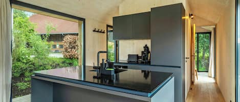 A modern kitchen with a central island, wooden ceiling, and large windows.