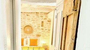 A narrow hallway leading to a bedroom with a stone wall, a bed with yellow bedding, and a rustic wooden door. - Village house with panoramic view in Venasque (Venasque)