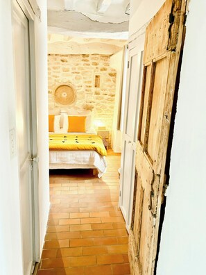 A narrow hallway leading to a bedroom with a stone wall, a bed with yellow bedding, and a rustic wooden door. - Village house with panoramic view in Venasque (Venasque)