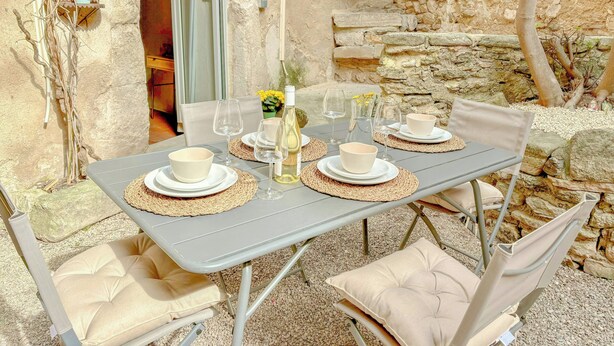 An outdoor dining area with a stone wall backdrop, a table set with white bowls and wine glasses, and cushioned chairs. - Village house with panoramic view in Venasque (Venasque)