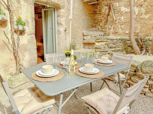 An outdoor dining area with a stone wall backdrop, a table set with white bowls and wine glasses, and cushioned chairs. - Village house with panoramic view in Venasque (Venasque)