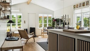 A modern kitchen with a central island, wooden flooring, and large windows. - Here, time is tuned into intimacy and coziness (Hadsund)