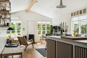 A modern kitchen with a central island, wooden flooring, and large windows. - Here, time is tuned into intimacy and coziness (Hadsund)