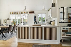 A modern kitchen with a central island, pendant lighting, and a dining area with a wooden table and chairs. - Here, time is tuned into intimacy and coziness (Hadsund)