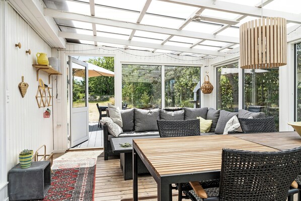 A covered patio with a wooden table, wicker furniture, and a sofa with cushions. - Here, time is tuned into intimacy and coziness (Hadsund)