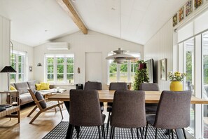 A spacious dining area with a wooden table and chairs, large windows, and a ceiling with exposed beams. - Here, time is tuned into intimacy and coziness (Hadsund)