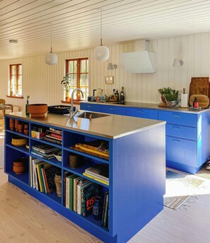 Eine Küche mit blauen Schränken, einer zentralen Kochinsel und einem Bücherregal voller Bücher.