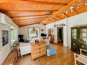 A cozy cabin interior with a wooden ceiling, a dining area, a kitchen, and a living space. - Holiday home with private garden in Ugglehult (Hjärnarp)