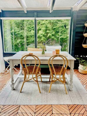A dining area with a table and chairs, a vase with flowers, and a view of greenery through large windows. - Holiday home with private garden in Ugglehult (Hjärnarp)