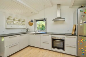 Eine moderne Küche mit weißen Schränken, einem eingebauten Backofen, einem Edelstahlkühlschrank und einem Fenster für natürliches Licht.