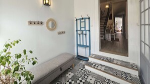 Un couloir avec un banc, un miroir fixé au mur, un luminaire et un chambranle de porte bleu.