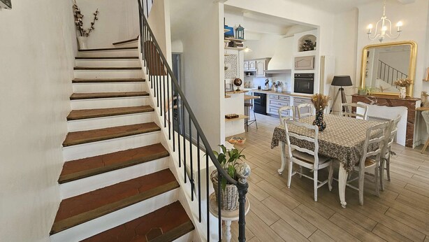 Un escalier menant à une salle à manger avec une table et des chaises, une cuisine en arrière-plan et un lustre.