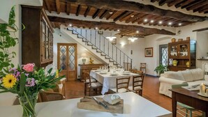 A dining area with a table set for four, a staircase, and a living room with a sofa. - Giglio. Country villa with private pool near Lucca (Lucca)