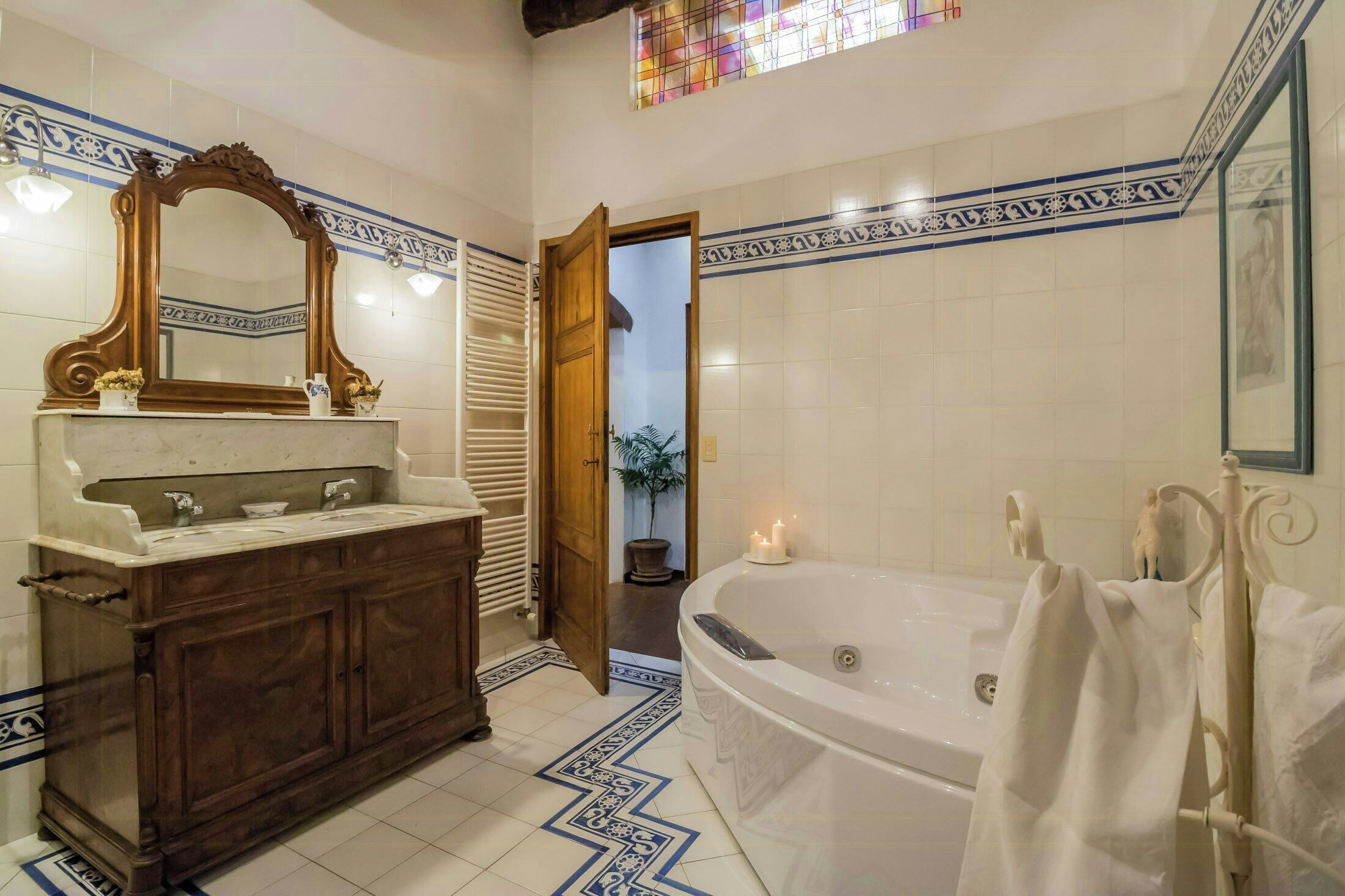 A bathroom with a large mirror, a wooden vanity, a bathtub, and a tiled floor with a geometric pattern.