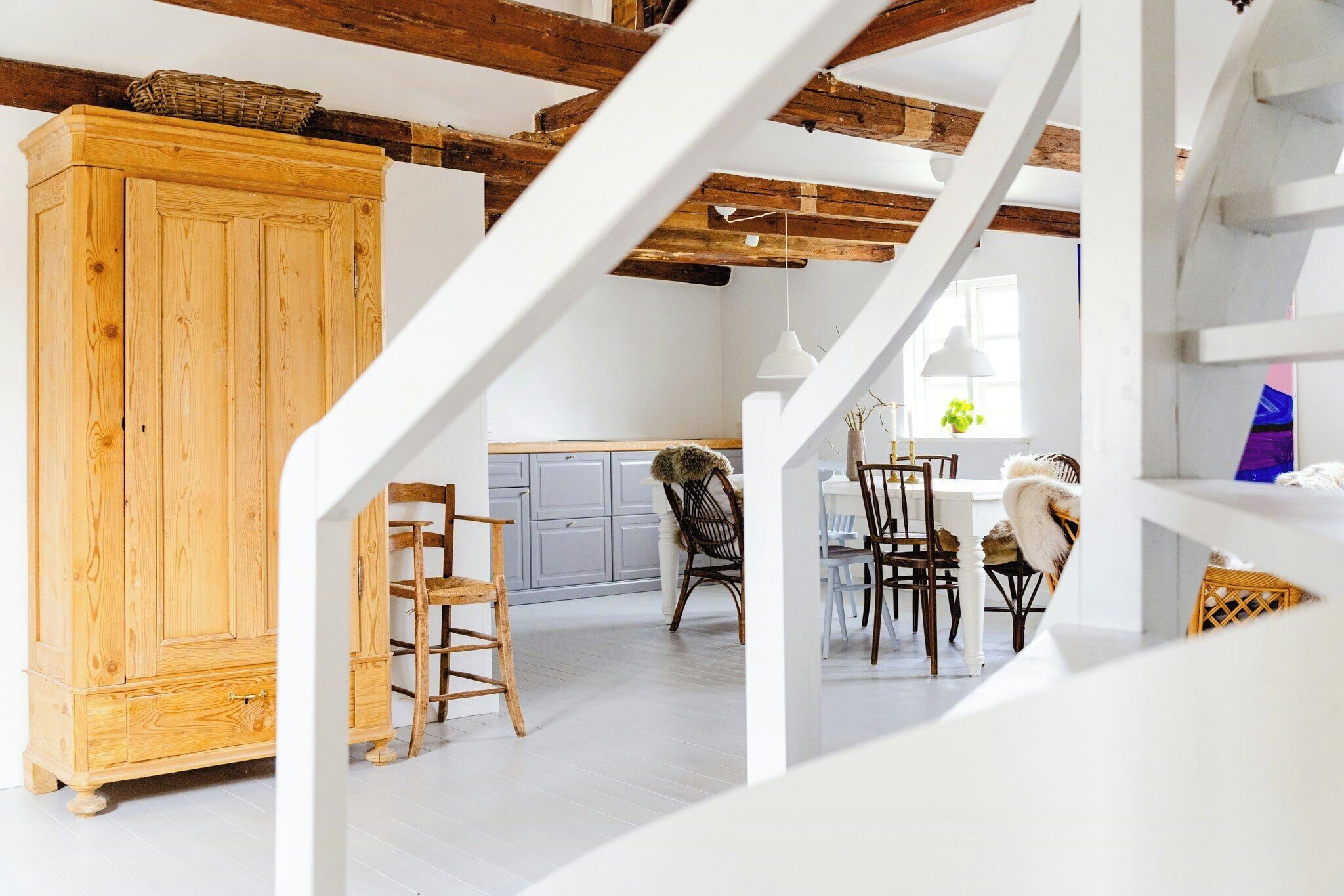 A spacious loft with exposed wooden beams, a wooden cabinet, and a dining area with chairs and a table.