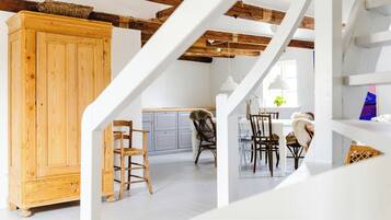 A spacious loft with exposed wooden beams, a wooden cabinet, and a dining area with chairs and a table.