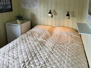 Ein Bett mit gesteppter Bettdecke, ein kleiner Nachttisch mit Pflanze, zwei Wandlampen und eine Wanduhr.