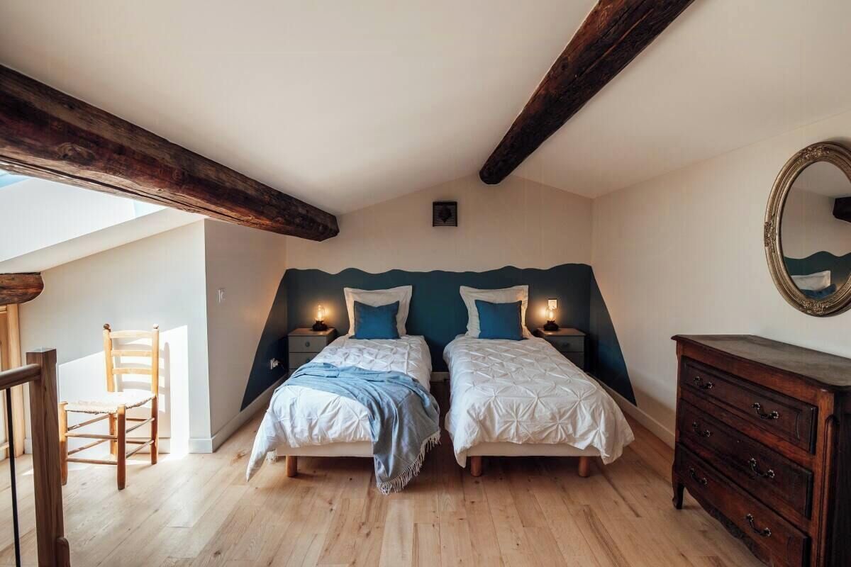 Een slaapkamer met twee bedden, houten balken, een kast en een spiegel.