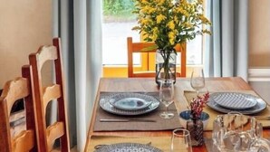 A dining table set for four with plates, cutlery, and glasses, a vase with yellow flowers, and a view of greenery through a window. - Charming house in an organic wine estate (Frontignan)