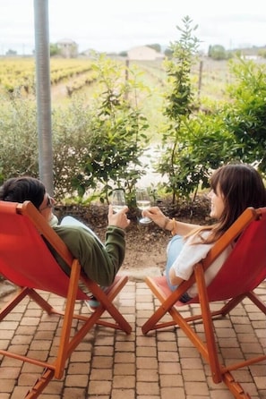 Deux personnes sont allongées sur des chaises rouges, sur une terrasse en briques, avec un vignoble en arrière-plan.