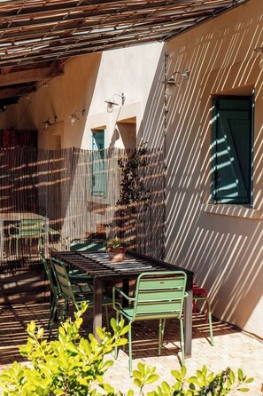 An outdoor patio with a table and chairs, a fence, and a building in the background. - Charming house in an organic wine estate (Frontignan)