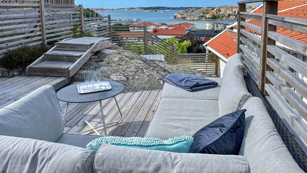 Un terrazza in legno con un divano e un tavolo, con vista su una località costiera con case e barche.