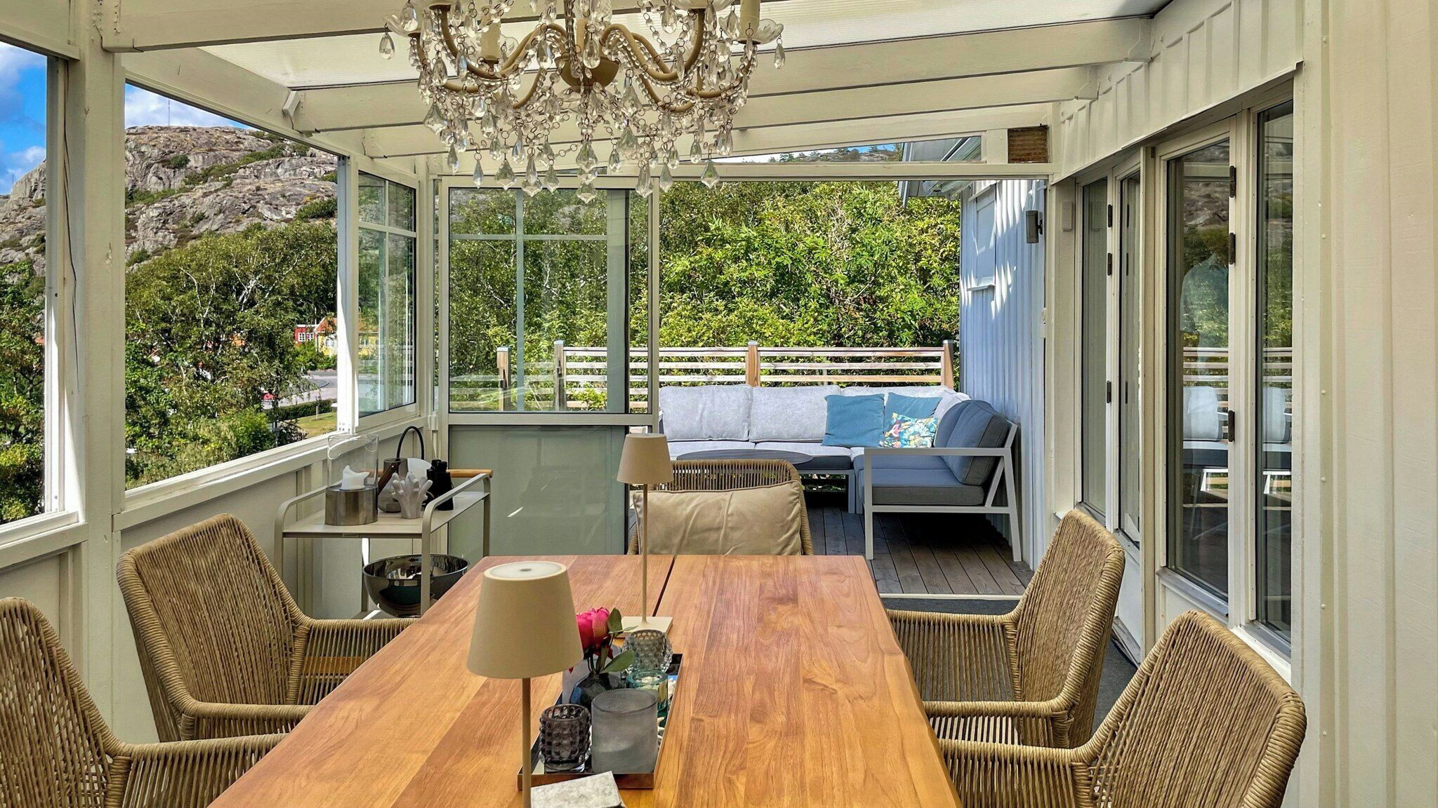 Une véranda avec une table en bois, des chaises en osier, un canapé et un lustre.