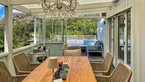 Una veranda con un tavolo in legno, poltrone in vimini, un divano e un lampadario.