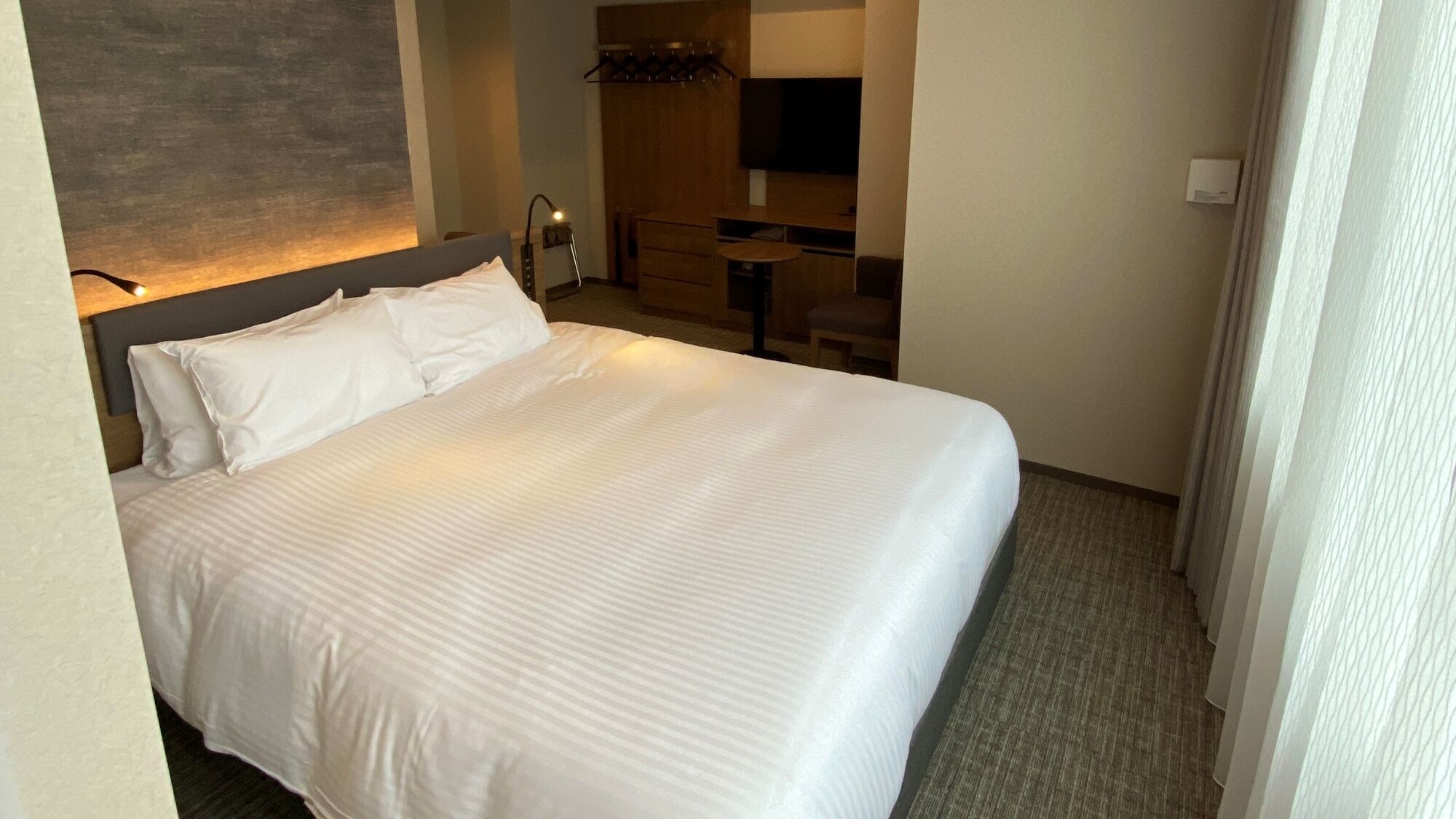 A hotel room with a large bed, a desk, a chair, a flat-screen TV, and a wooden cabinet.